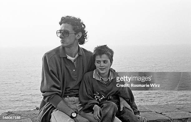 young father and son sitting in front of sea, spring 1983. - italien familie stock-fotos und bilder