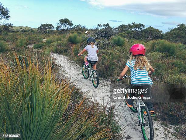 children riding bikes on sandy track with father - two kids with cycle stock-fotos und bilder
