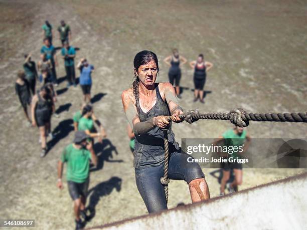 woman using a knotted rope to climb a large wall - mud run ストックフォトと画像