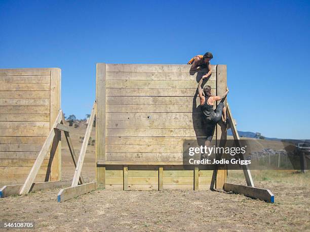 women climbing large wall during obstacle course - climbing help stock-fotos und bilder