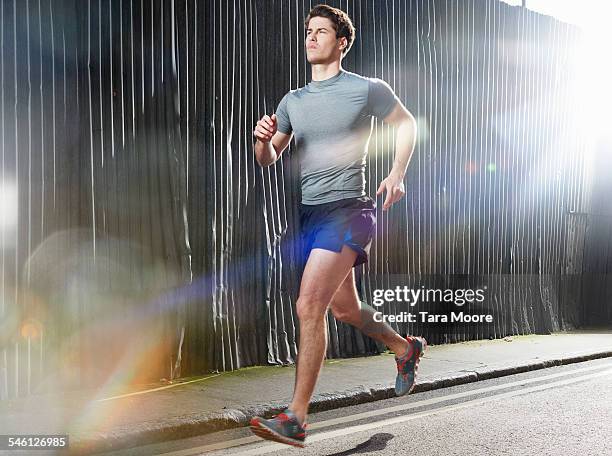 man running on sunny street in urban setting - running shorts stockfoto's en -beelden