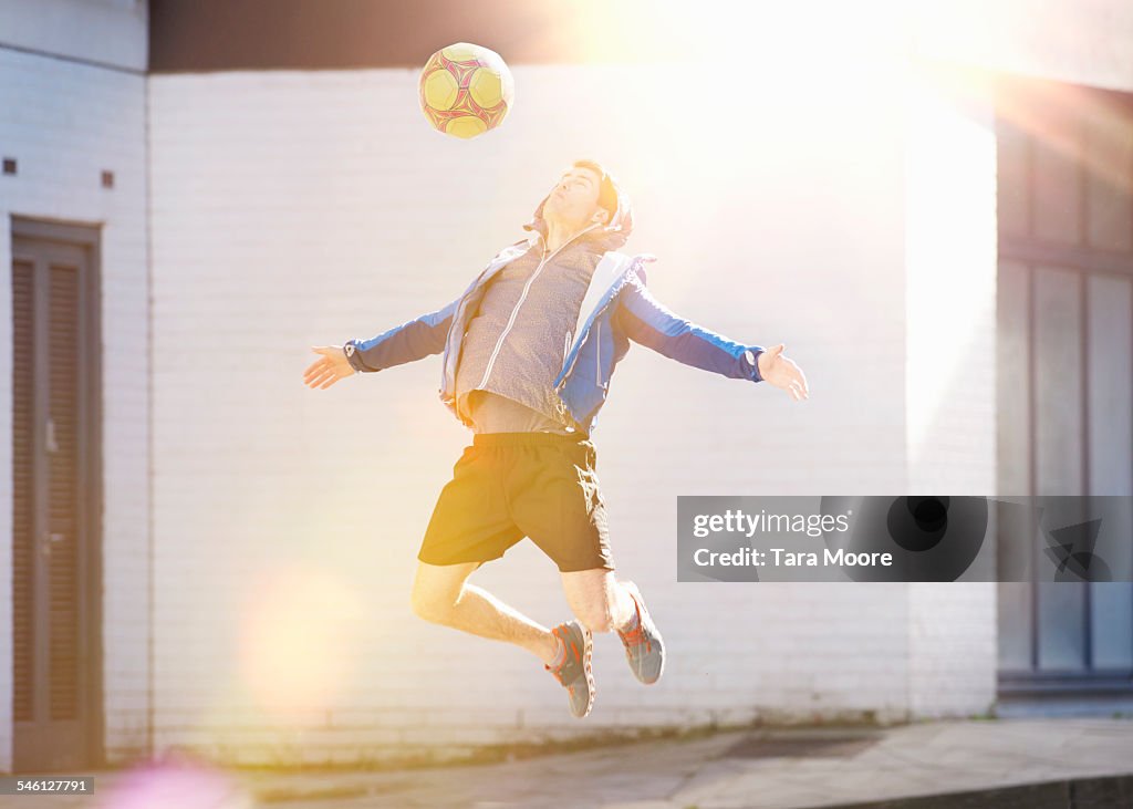 Sportsman jumping in air with football in street