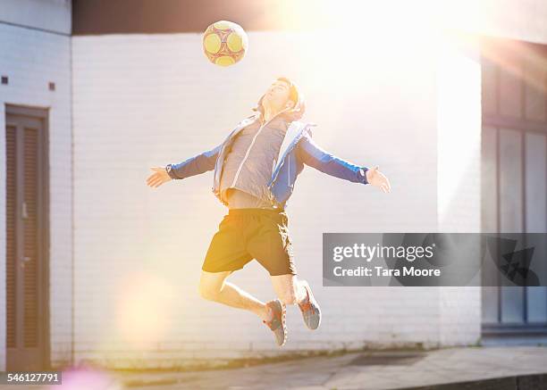 sportsman jumping in air with football in street - street football stock pictures, royalty-free photos & images