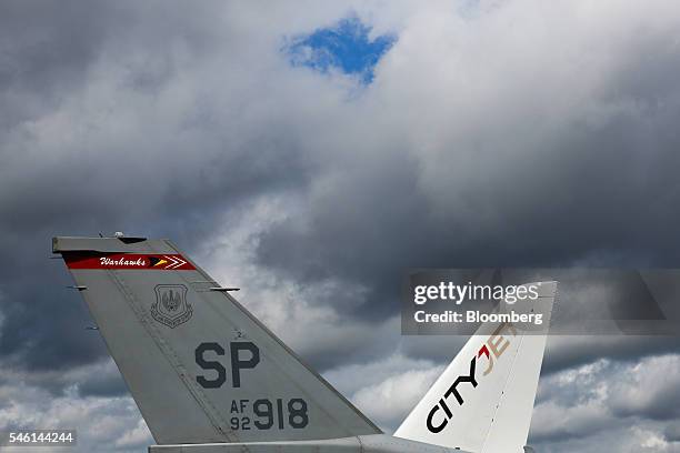 The tail fins of a Lockheed Martin Corp. F-16, left, and Sukhoi Civil Aircraft Co. Superjet 100 aircraft, operated by CityJet Ltd., on the opening...