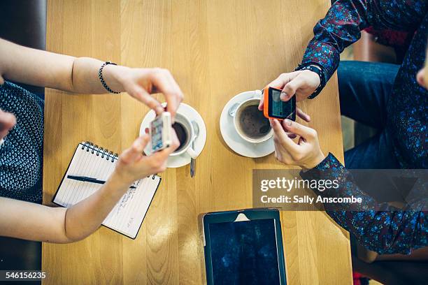 two teenagers using smart phones - sharing coffee stockfoto's en -beelden