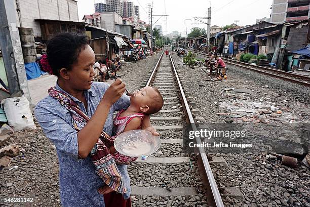 Woman give her baby food near the railway tracks at the Slum area on July 09, 2016 in Jakarta, Indonesia. Indonesia is the most populous country in...