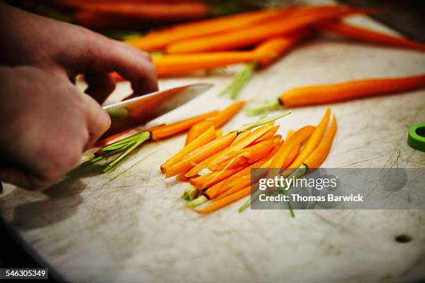 man slicing carrots on cutting board in kitchen - diet carrot stock-fotos und bilder