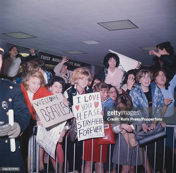 Teenage girls and fans of English pop group The Beatles shout and cheer and hold welcome signs as they wait for the group to arrive at Kennedy...