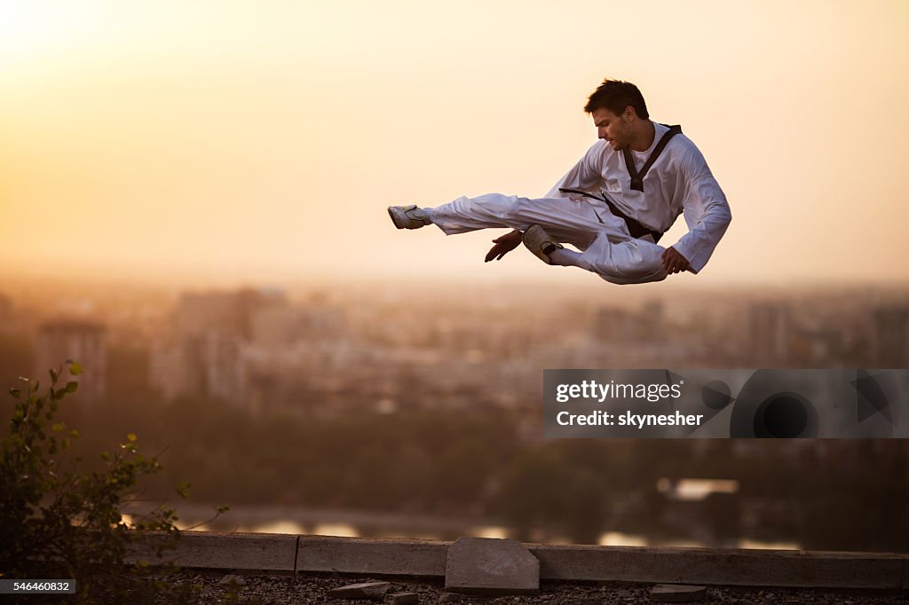 Kampfkünstler mit hohem Kick in der Luft bei Sonnenuntergang.