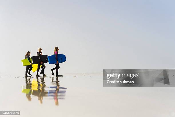 mujeres caminando en la playa con sus bodyboards - bodyboard fotografías e imágenes de stock