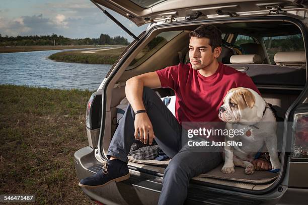 young man sitting on car's tail with bulldog - red trousers stock-fotos und bilder