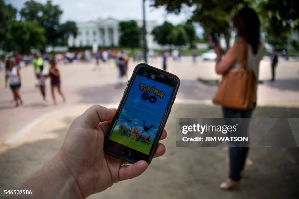 Man holds up his cell phone with a screen shot of the Pokemon Go game as a woman searches on her cell phone for a Pokemon in front of the White House...