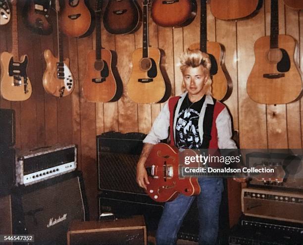 Musician Brian Setzer of "Stray Cats" poses for a portrait on Polaroid film with a guitar in front of a wall of guitars and amps including, a...