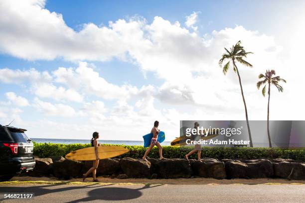 pacific islander surfers carrying surfboards on rock wall - woman side view walking stock pictures, royalty-free photos & images