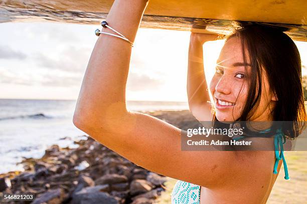 pacific islander surfer carrying surfboard on rocky beach - forte beach photos et images de collection