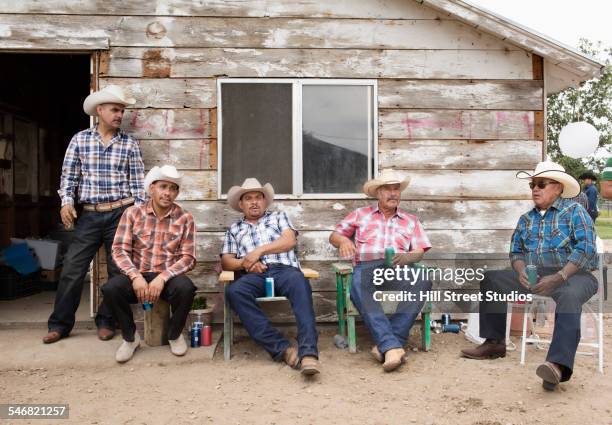 hispanic men in cowboy hats relaxing near shed - cowboy hat imagens e fotografias de stock