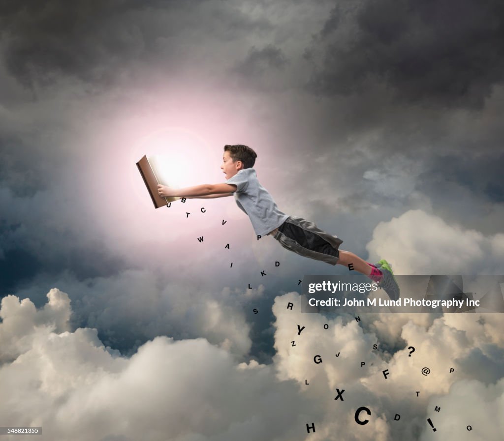 Caucasian boy flying with book in sky