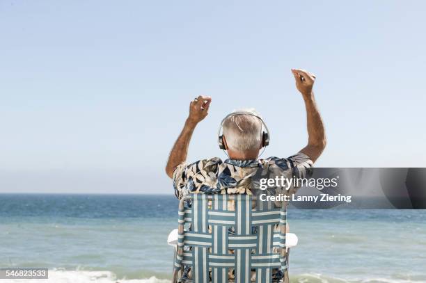 older man listening to headphones on beach - beach music stock pictures, royalty-free photos & images