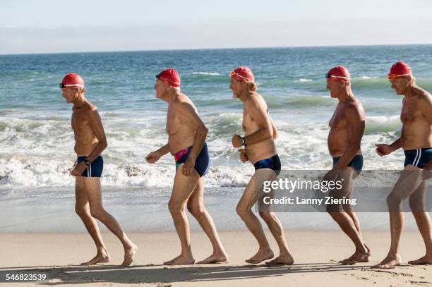 older men on swimming team running on beach - calções de corrida imagens e fotografias de stock