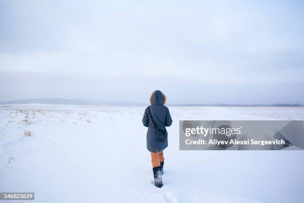 caucasian woman walking in snowy field - parka coat stockfoto's en -beelden