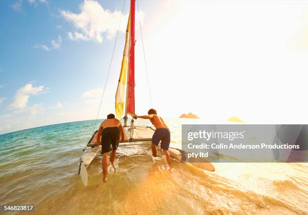 caucasian men pushing sailboat into ocean from beach - hawaii fun fotografías e imágenes de stock