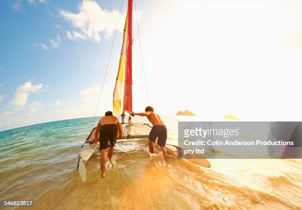 caucasian men pushing sailboat into ocean from beach - summer press day ストックフォトと画像