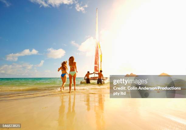 women running on beach to sailboat in ocean - hawaii fun stock-fotos und bilder