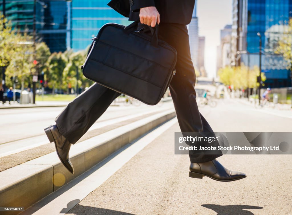 Caucasian businessman carrying briefcase across city street