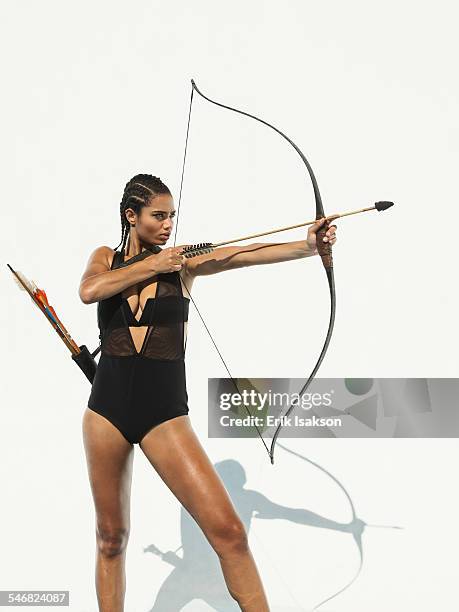 mixed race woman aiming bow and arrow - bogen pfeil und bogen stock-fotos und bilder