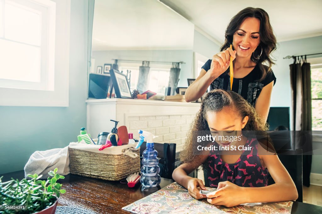 Mother combing hair of daughter at kitchen table