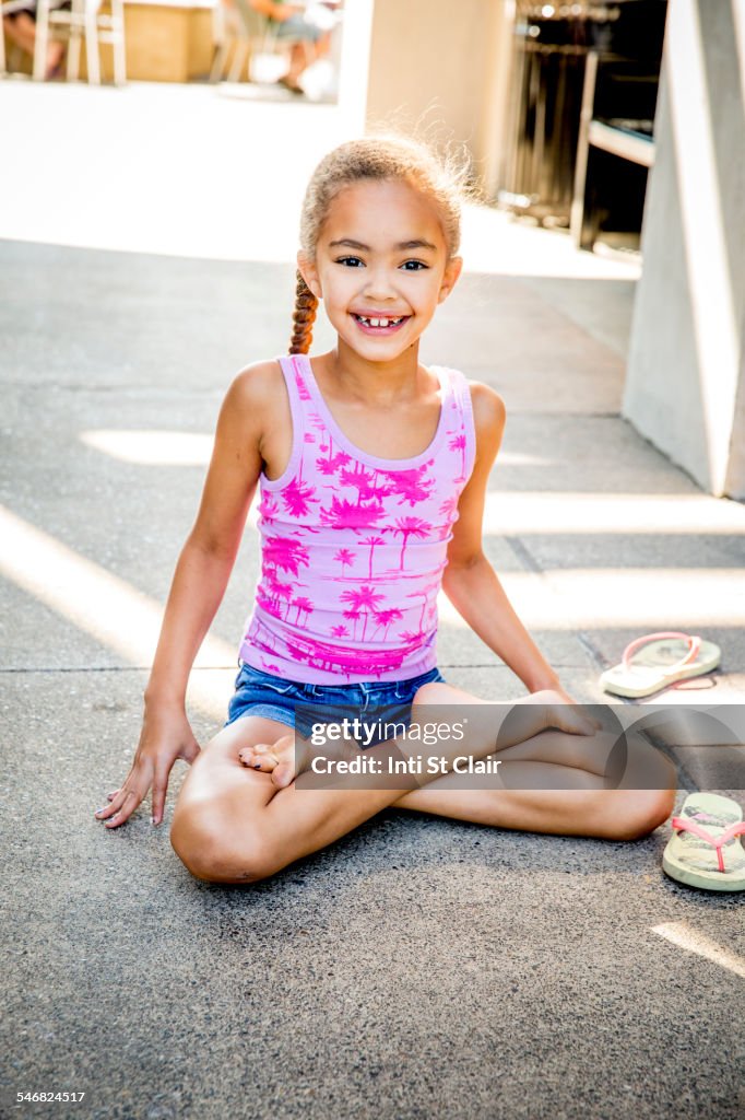 Mixed race girl sitting with legs crossed on sidewalk