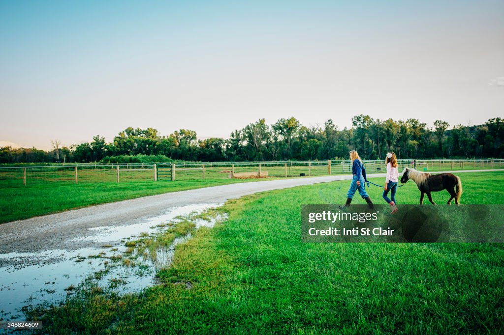 Caucasian mother and daughter walking miniature horse on farm