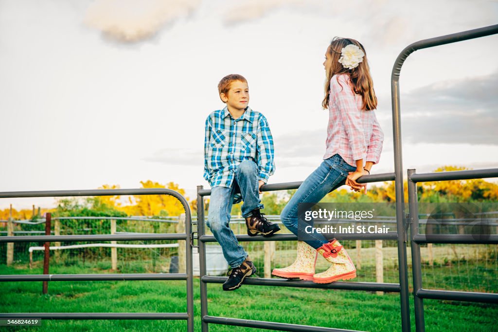 Caucasian children sitting on fence on farm