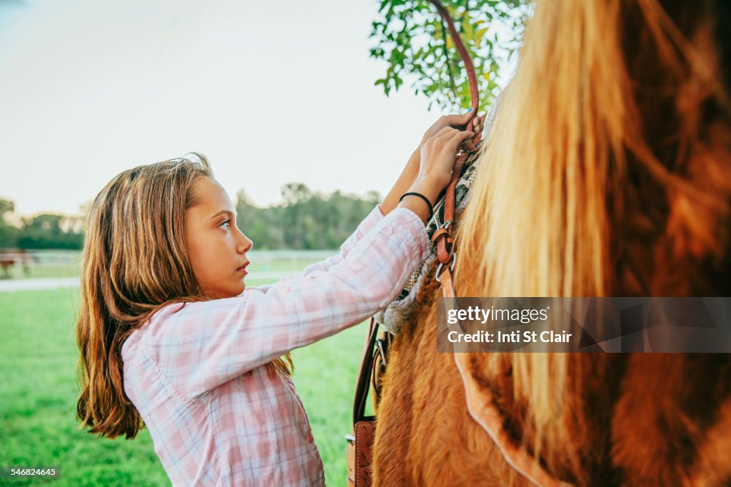 Caucasian girl fastening saddle on horse