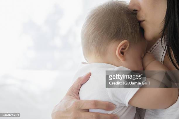 close up of mixed race mother kissing baby on forehead - cara oculta fotografías e imágenes de stock