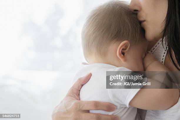 close up of mixed race mother kissing baby on forehead - no face stock pictures, royalty-free photos & images