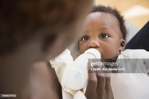 close up of black mother feeding baby boy - drinking from bottle stock pictures, royalty-free photos & images