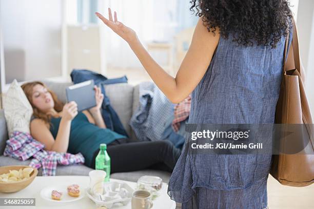 woman frustrated at lazy roommate using digital tablet on sofa - friends argue fotografías e imágenes de stock