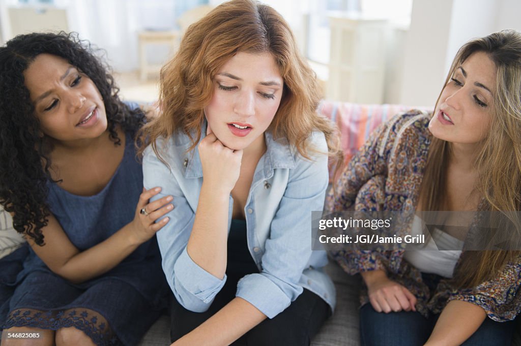 Women comforting sad friend on sofa in living room