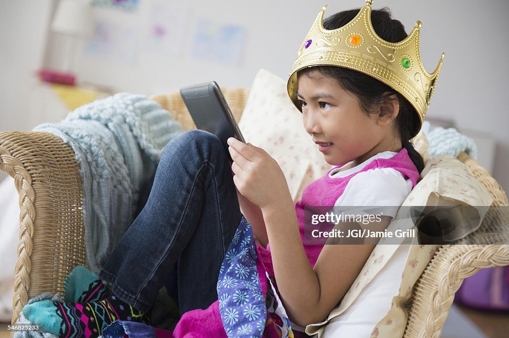 Vietnamese girl with crown using digital tablet in armchair