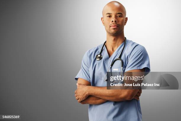 mixed race nurse standing with arms crossed - mixed race man standing studio stockfoto's en -beelden
