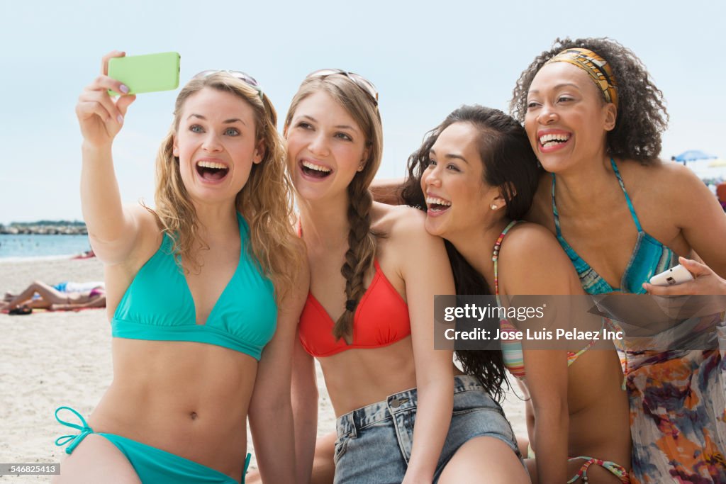 Smiling women taking cell phone photograph on beach