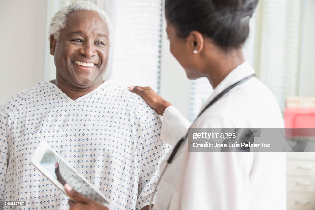 Doctor with digital tablet comforting older man in hospital