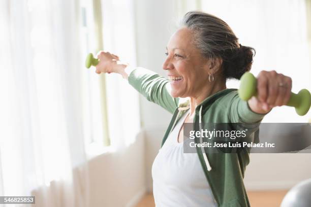 older hispanic woman lifting weights in living room - women working out stock pictures, royalty-free photos & images