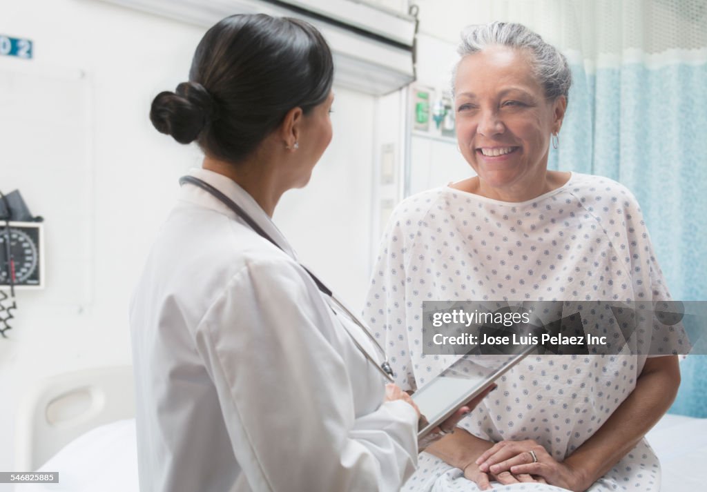 Hispanic doctor using digital tablet and talking to older patient