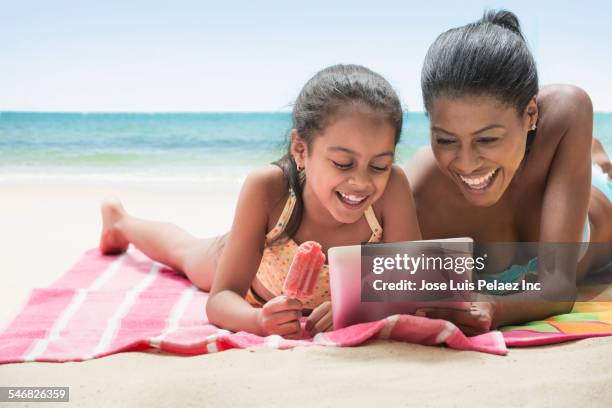 hispanic mother and daughter using digital tablet on beach - mother daughter towel fotografías e imágenes de stock