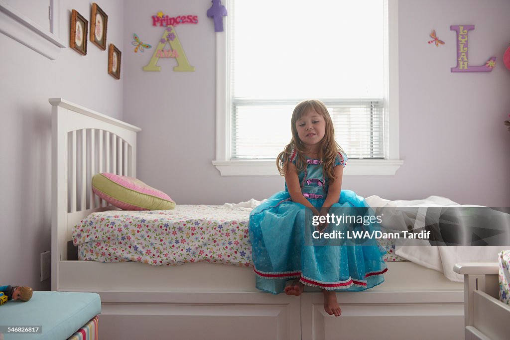 Caucasian girl in princess costume sitting on bed