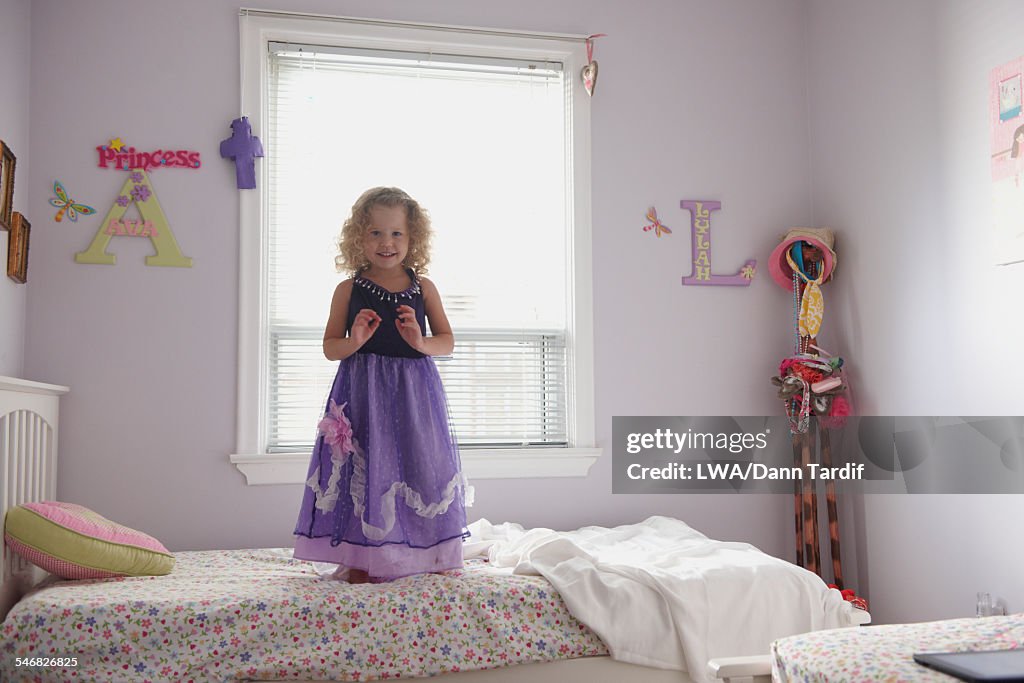 Caucasian girl in princess costume standing on bed