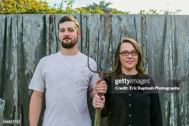 caucasian couple holding pitchfork near fence - american gothic stock-fotos und bilder