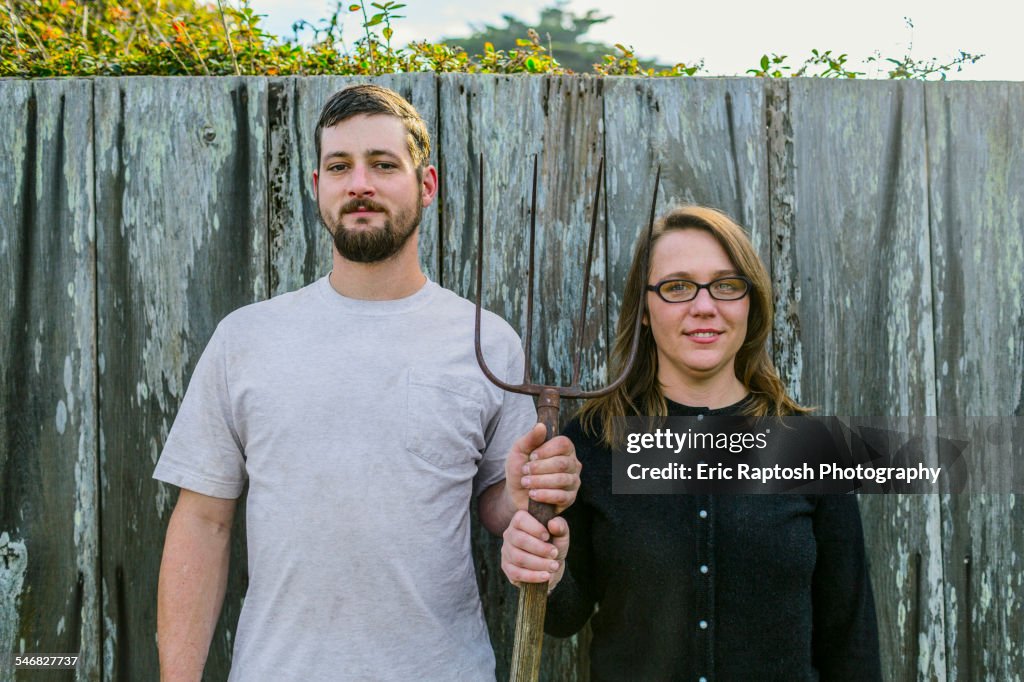 Caucasian couple holding pitchfork near fence